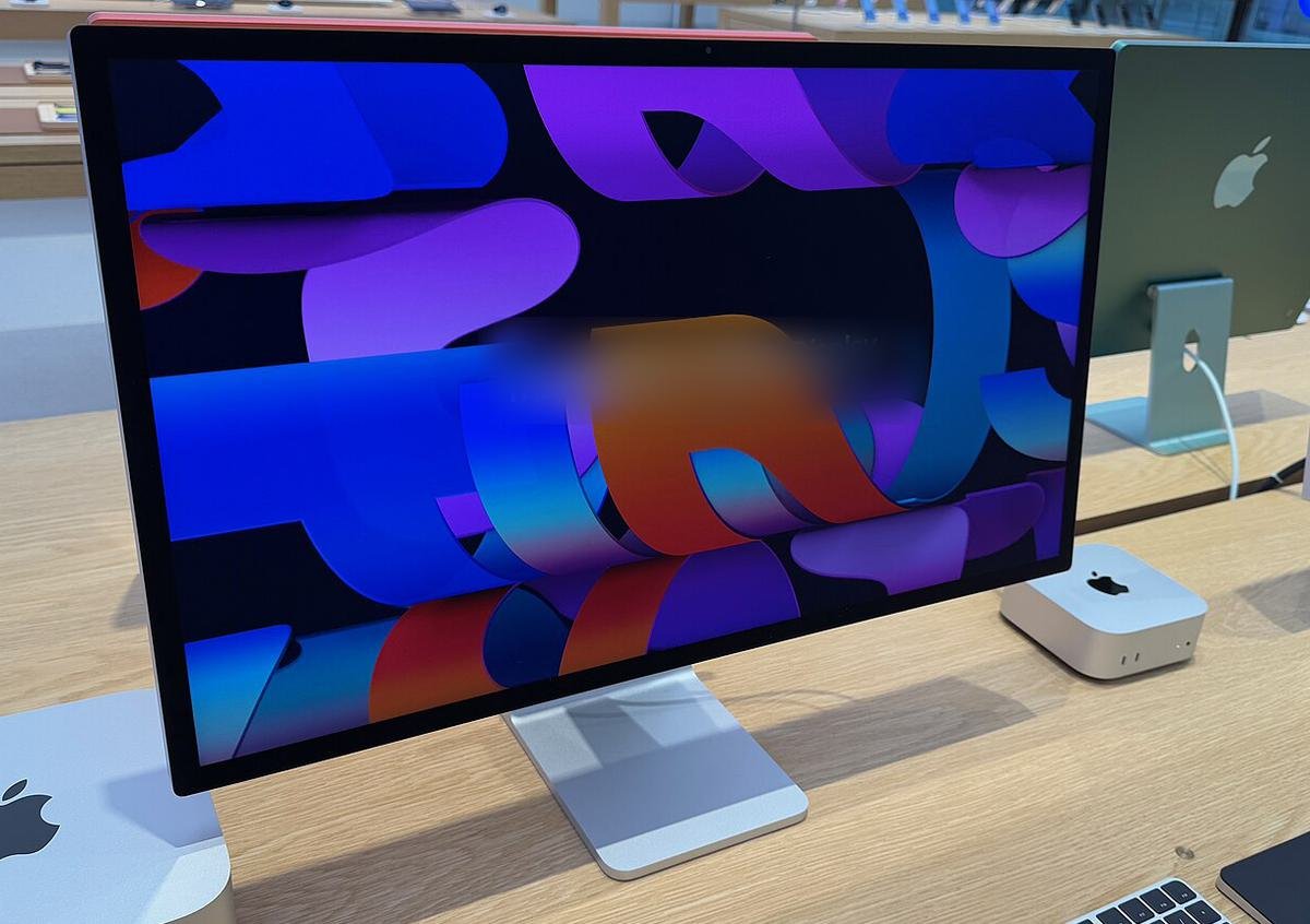A 27-inch monitor on a wooden desk with a small silver Mac mini beside it